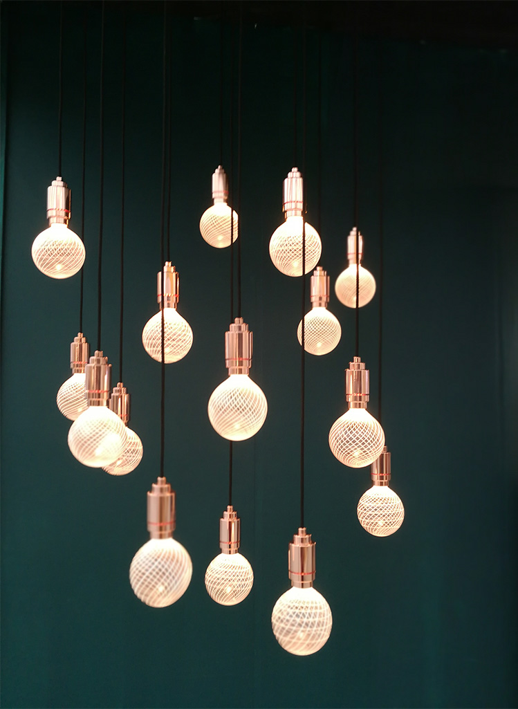 a photo of a very dark green wall with a brass light fitting with many bulbs in front of it.