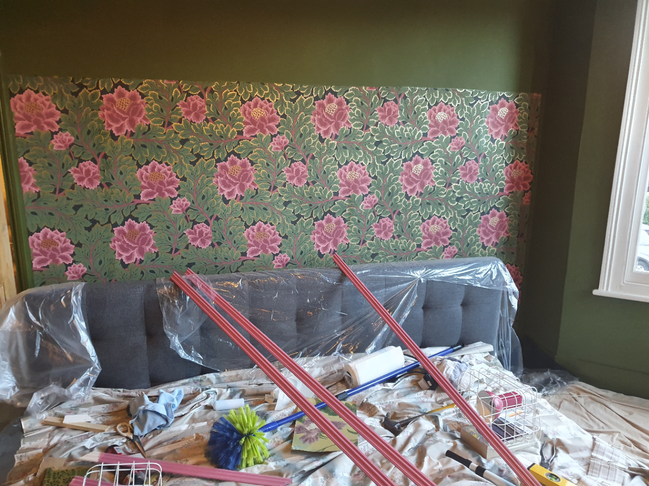 A photo of the wallpaper on the wall, with the pink beading on the bed ready to go up.
