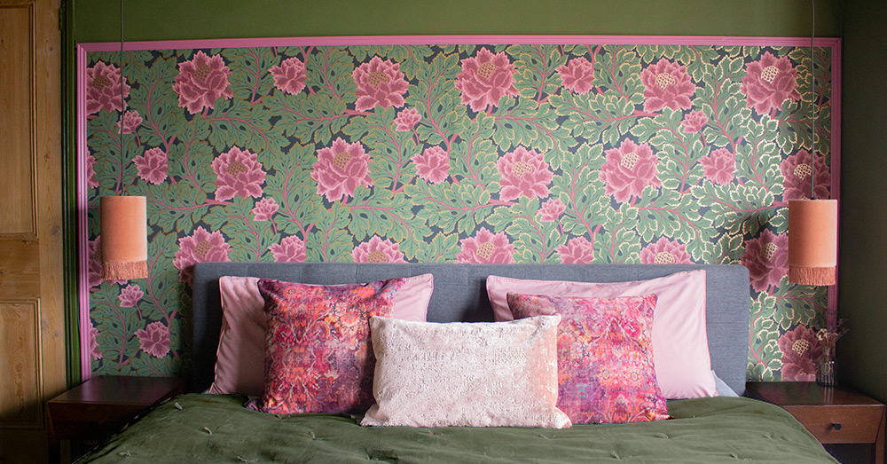 A close up of the bed with pink and green wallpaper behind and dark green walls.
