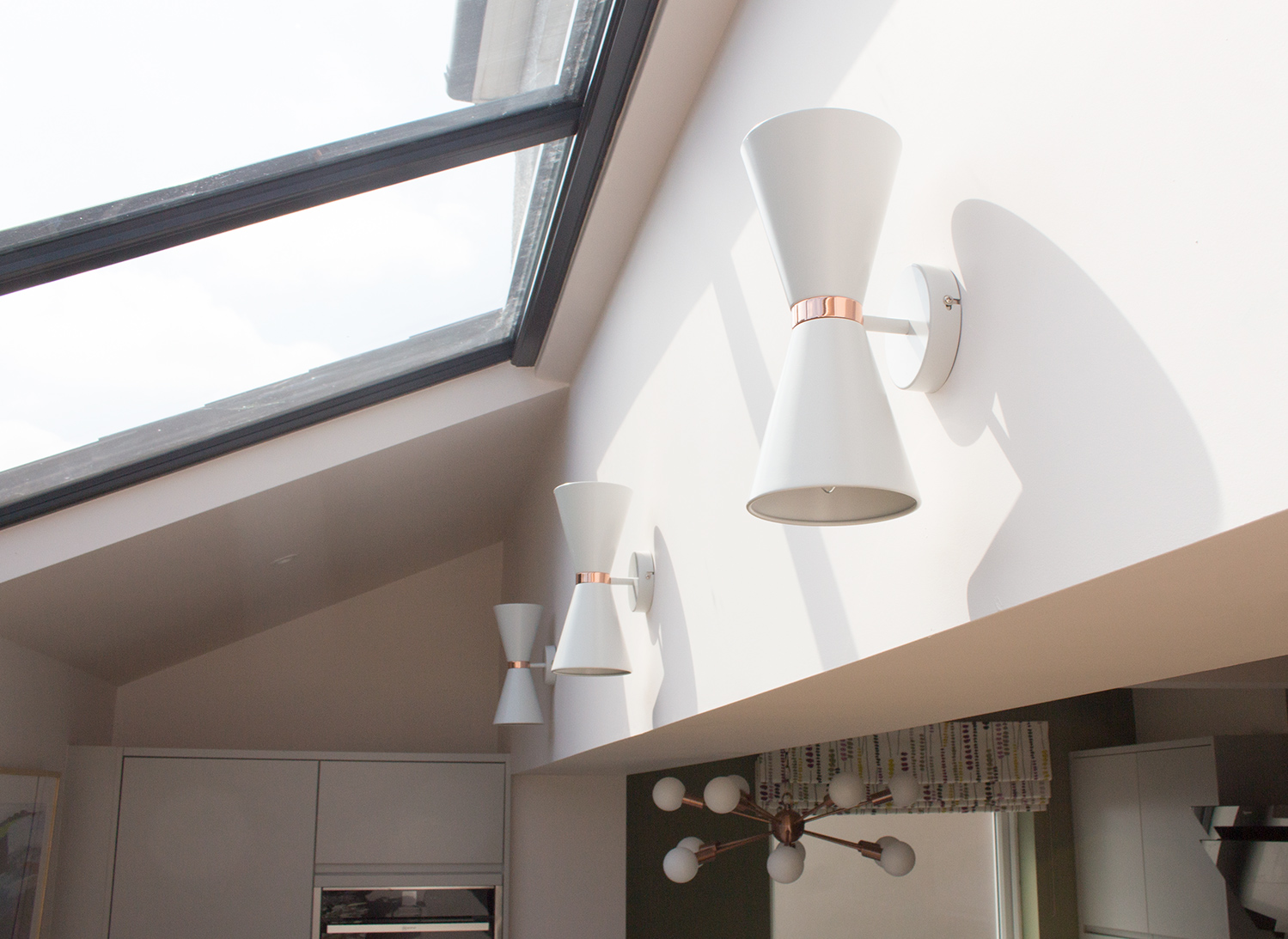 A photo of three wall lights with an interesting shape on a blank wall in a kitchen.