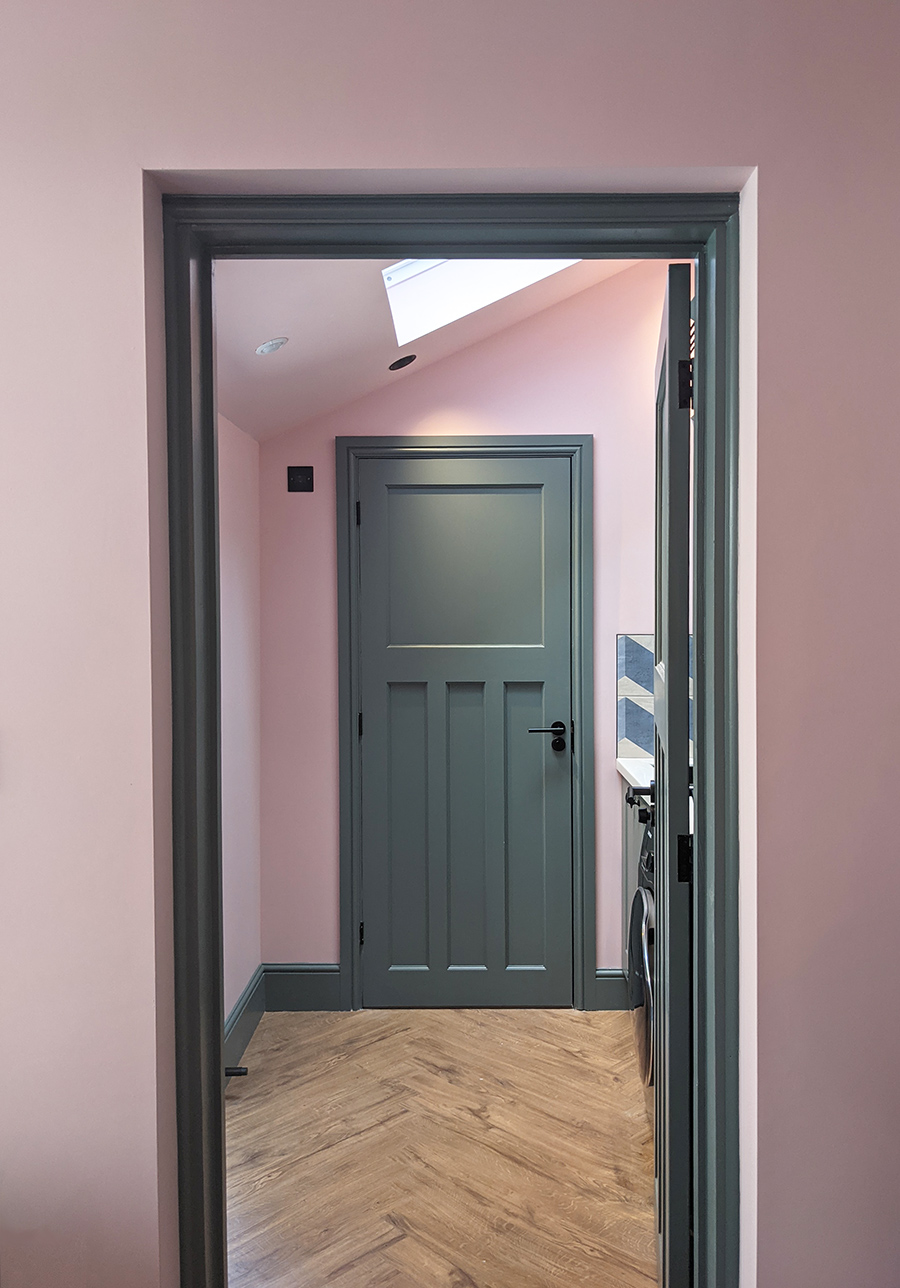 A photo of a utility room with pink walls, with the doors and trims picked out in a grey green.